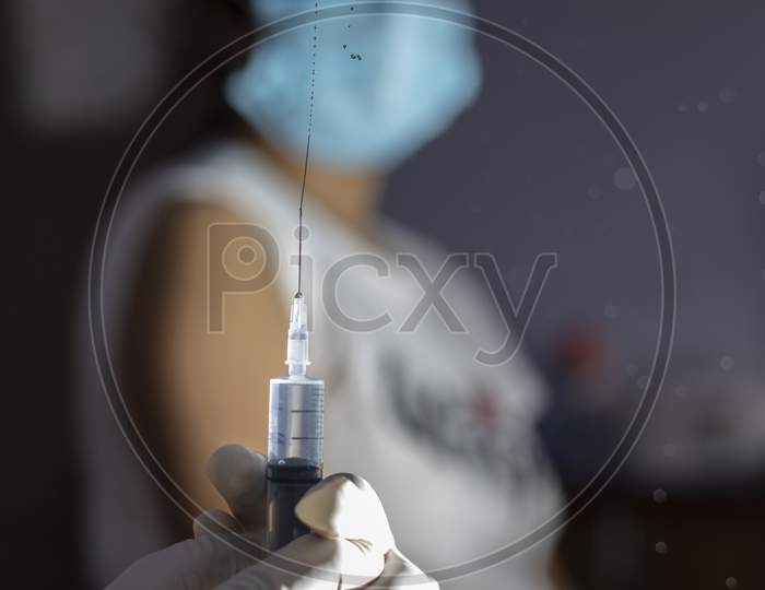 Selective Focus On An Injection Syringe In Hands While A Blurred Woman In Background Looks On