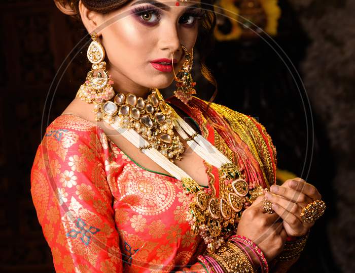 Portrait Of Very Beautiful Young Indian Bride In Luxurious Bridal Costume With Makeup And Heavy Jewellery In Studio Lighting Indoor. Wedding Fashion.