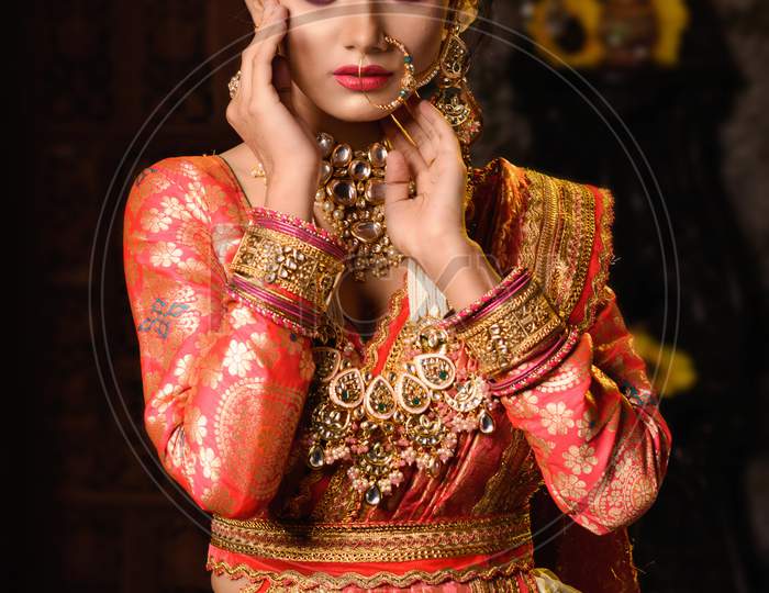 Portrait Of Very Beautiful Young Indian Bride In Luxurious Bridal Costume With Makeup And Heavy Jewellery In Studio Lighting Indoor. Wedding Fashion.