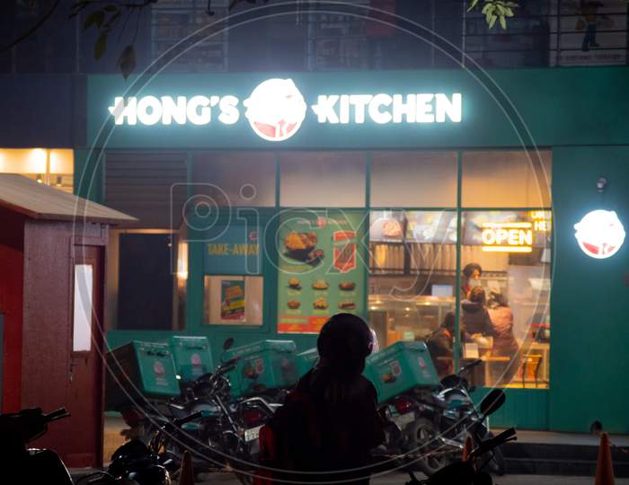 Lit Hongs Kitchen Storefront From Jubiliant At Night With Delivery Men Lining Up For Takeaway Meals In India