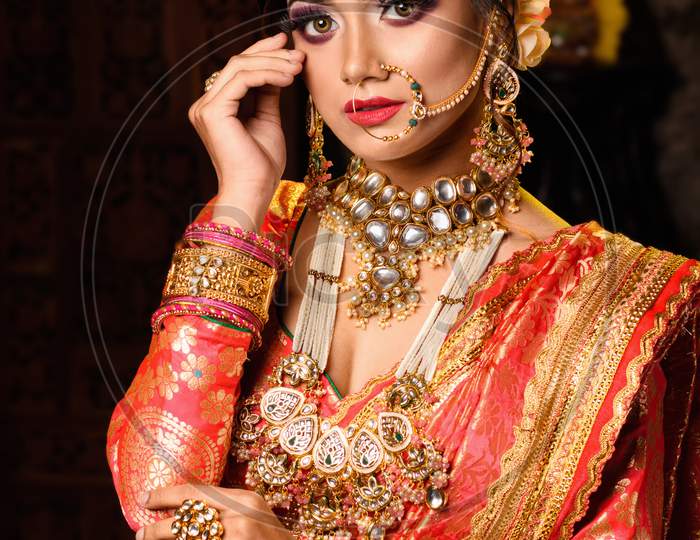 Portrait Of Very Beautiful Young Indian Bride In Luxurious Bridal Costume With Makeup And Heavy Jewellery In Studio Lighting Indoor