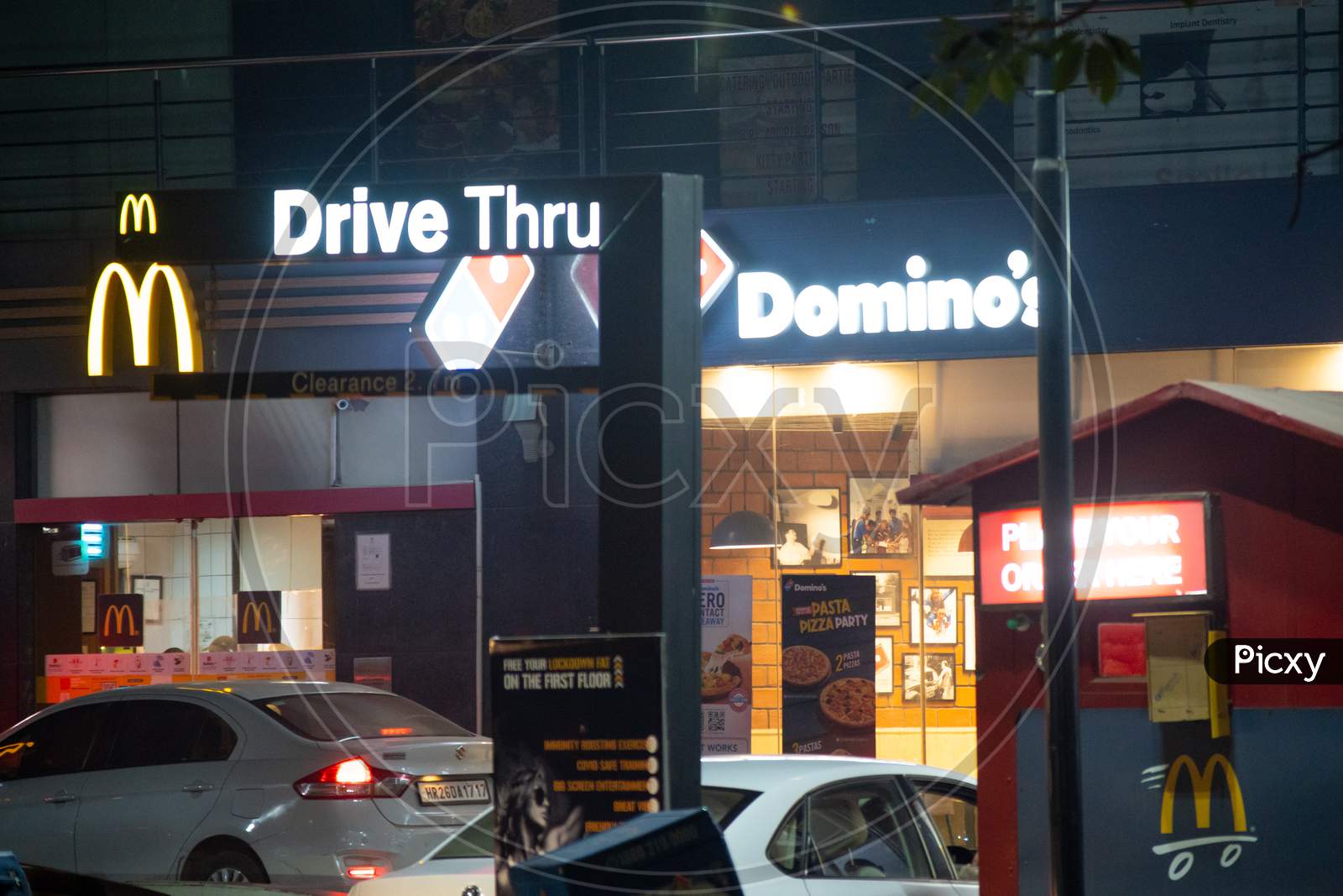 Lit Signboard For A Dominoes And Mcdonalds On A Busy Indian Street With Cars Lining Up For Takeaway From The Fast Food Quick Service Restaurant