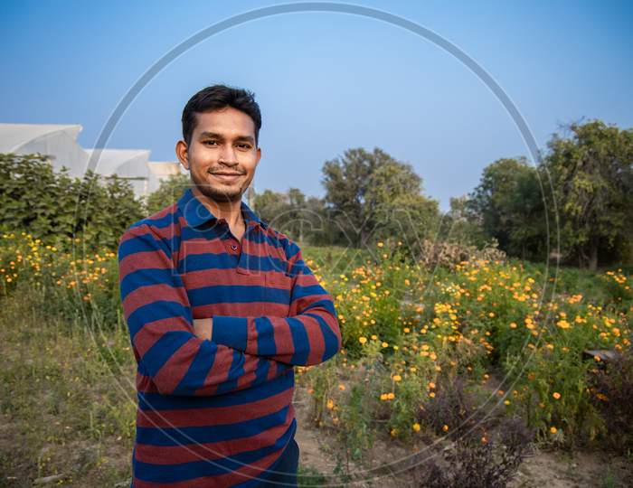 Portrait Of Young Smiling Indian Farmer Standing At Hi Farm, Copy Space, Man With Cross Arm. Agriculture.