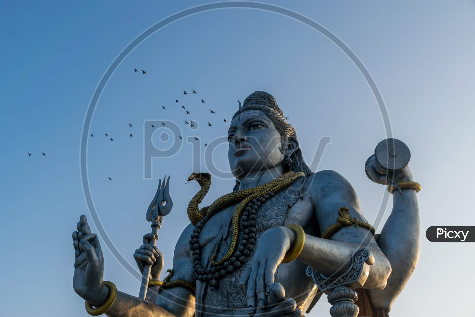 Landscape View Of The Second Tallest Lord Shiva Statue In The World With A Flock Of Flying Birds In Murdeshwar, Karnataka, India