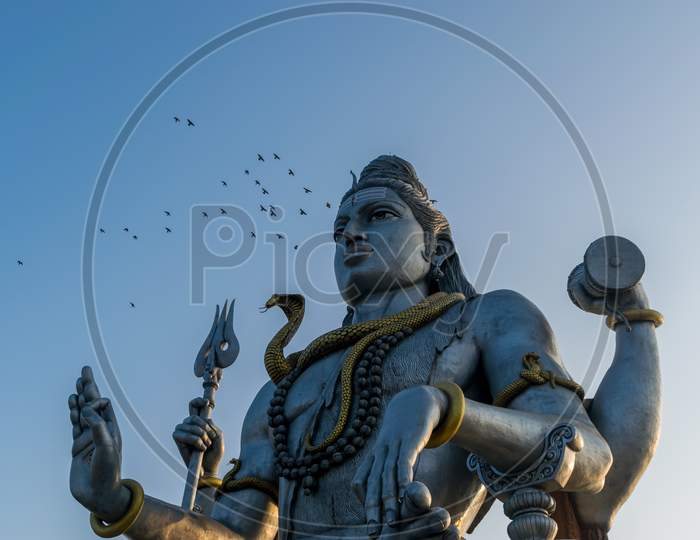 Landscape View Of The Second Tallest Lord Shiva Statue In The World With A Flock Of Flying Birds In Murdeshwar, Karnataka, India