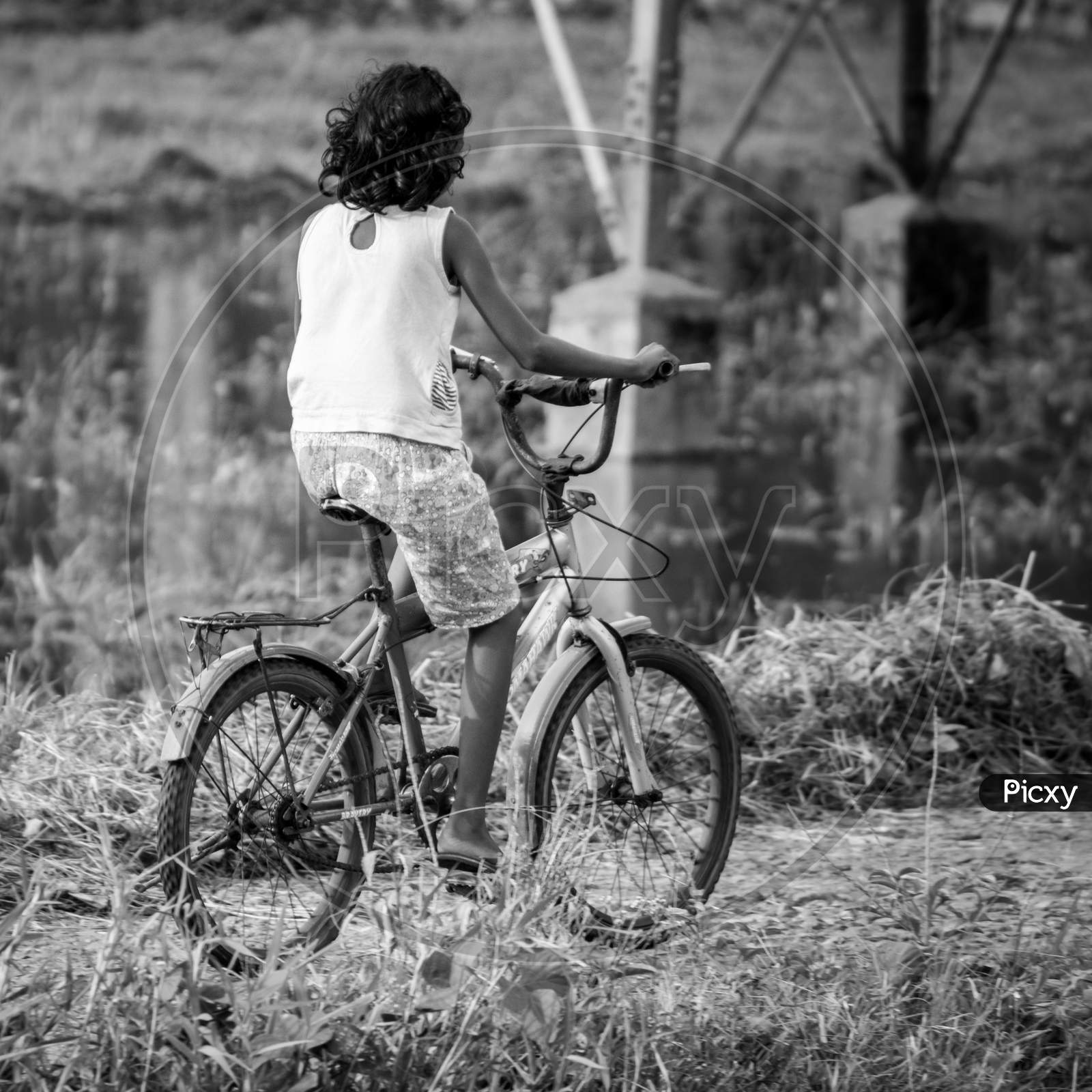 Small Girl Riding A Bicycle In A Rural Village Road, Beautiful Memories Of Childhood Concept, Black And White Photograph.