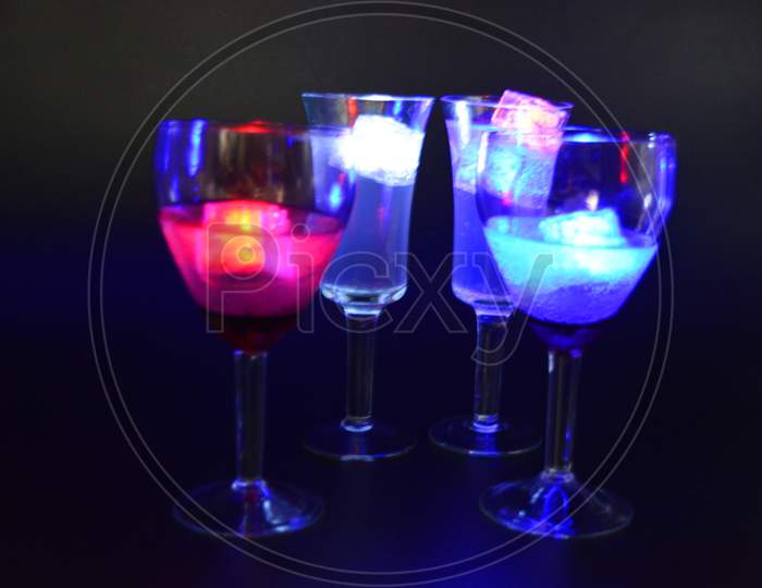 Four glasses with bright different colors of luminous led ice cubes are located on a black background.