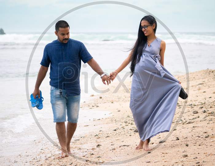 Relaxing And Enjoying Walking On The Beach Barefoot, Happy Couple Holding Hands And Having A Small Discussion, Young And Pregnant, Couple Goals Concept.