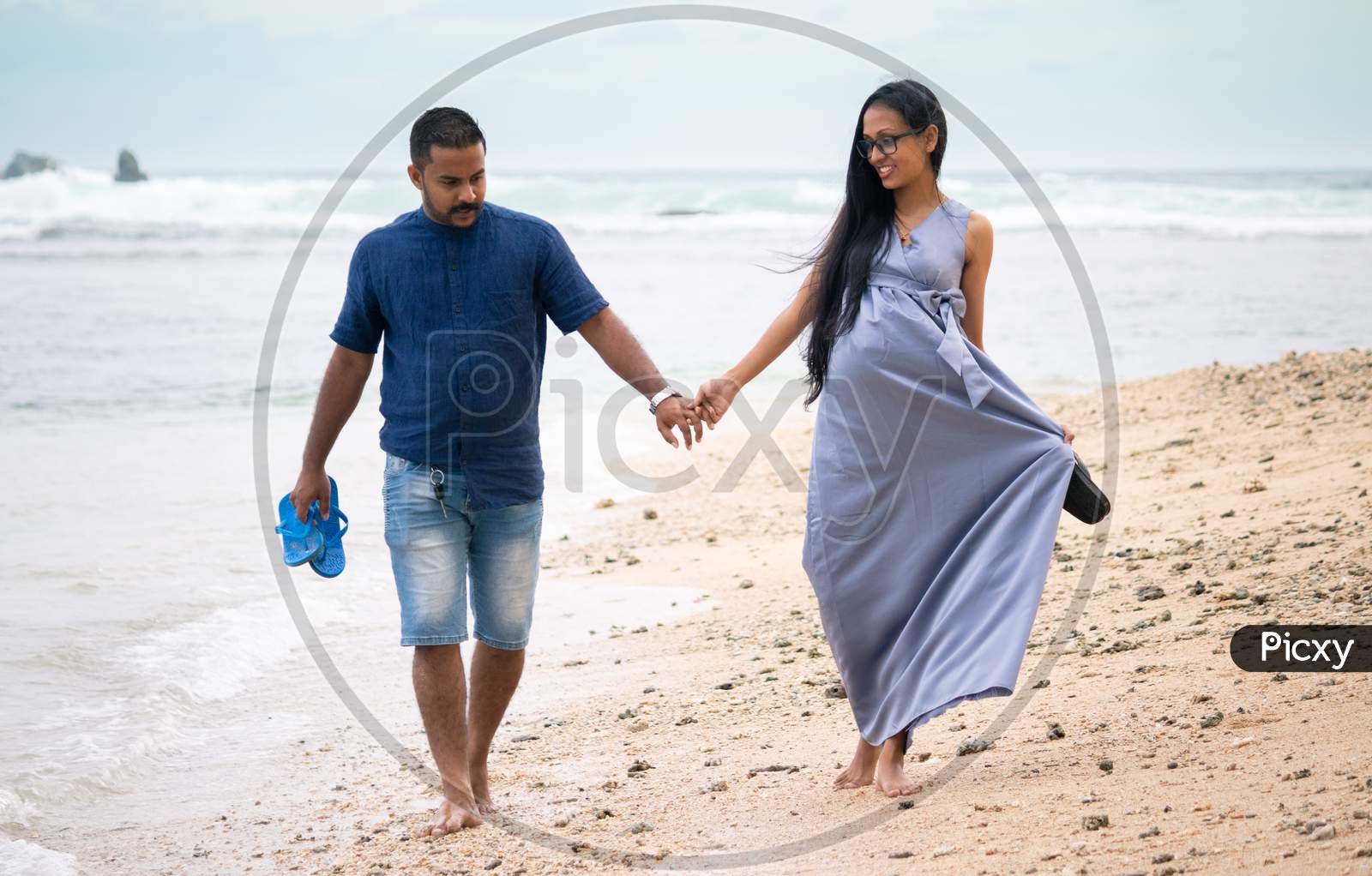 Relaxing And Enjoying Walking On The Beach Barefoot, Happy Couple Holding Hands And Having A Small Discussion, Young And Pregnant, Couple Goals Concept.