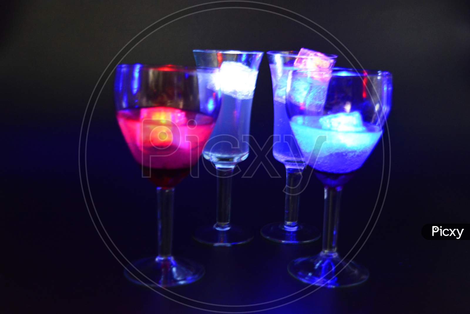 Four glasses with bright different colors of luminous led ice cubes are located on a black background.