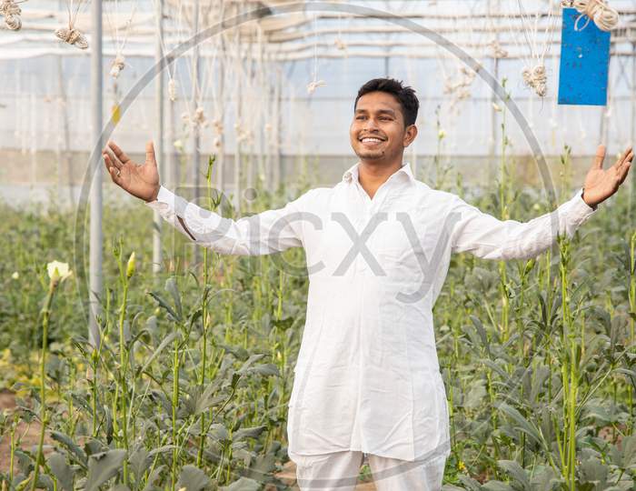 Young Happy Indian Farmer Standing With Open Arms At His Poly House Or Greenhouse, Agriculture Business And Rural Prosperity Concept. Man Wearing White Kurta Pajama Cloths, Copy Space.