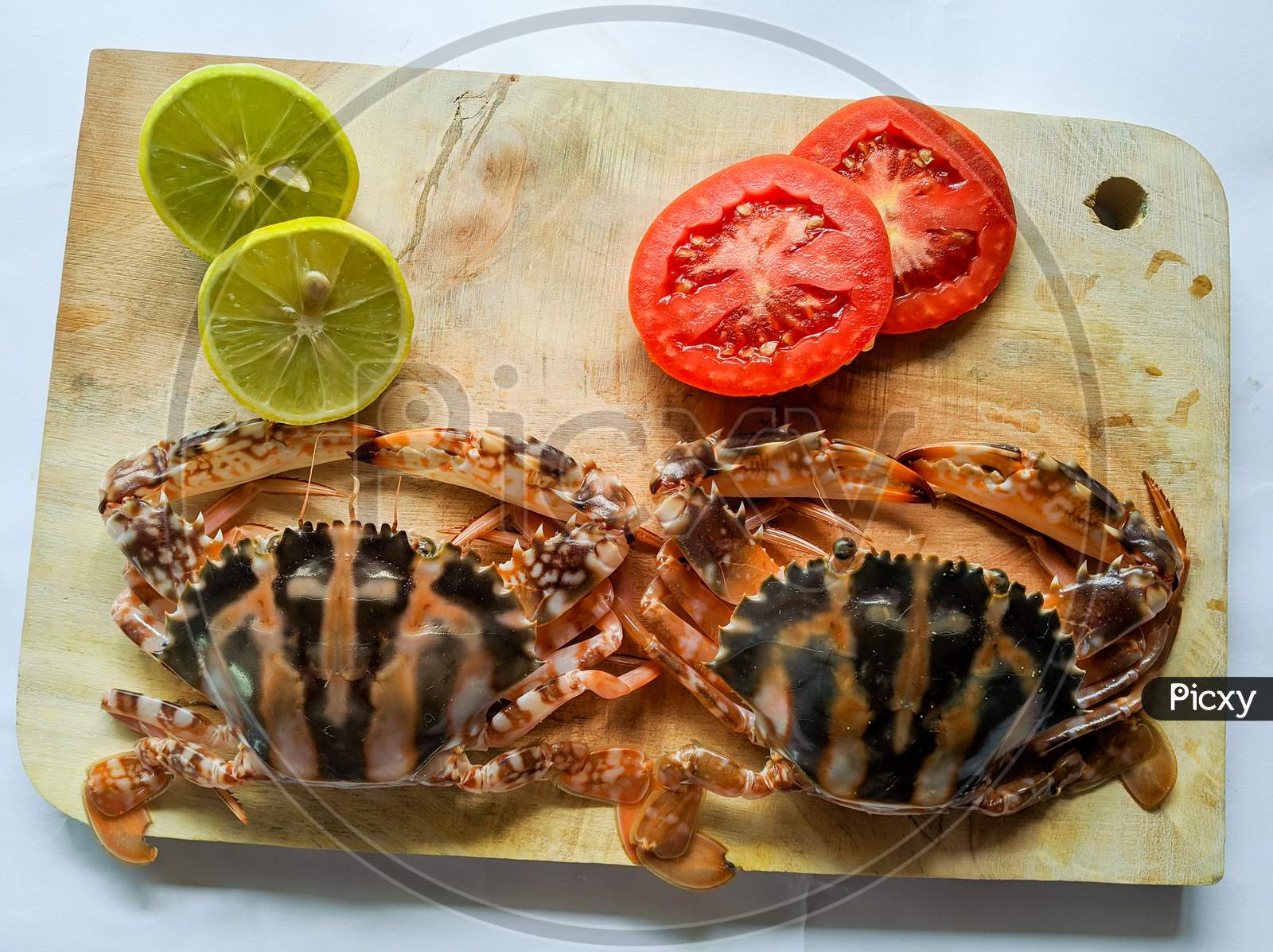 Selective Focus Of Fresh Crucifix Crab Decorated With Lemon Slice And Tomato Slice On A Wooden Pad.White Background