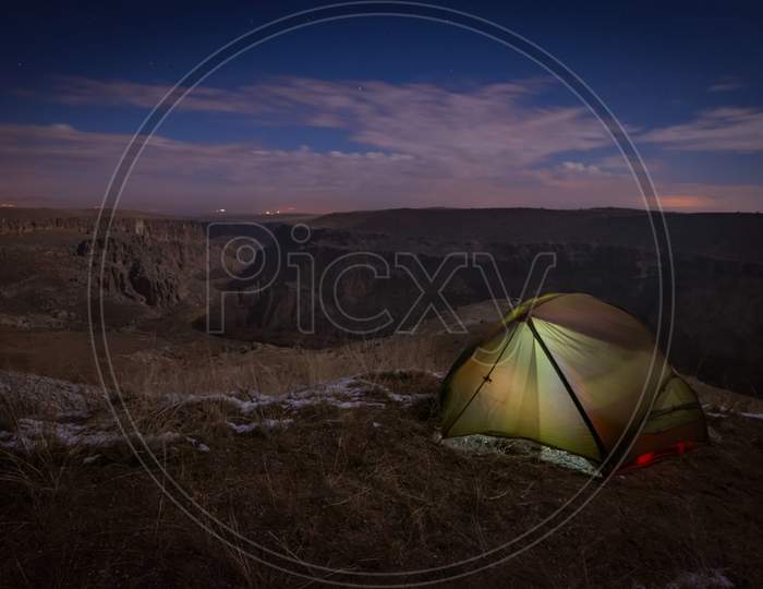 Green Tent Illuminated On Grass Surface With Snow And Stunning Ihalar Valley Background At Night. Wild Camping In Beautiful Locations