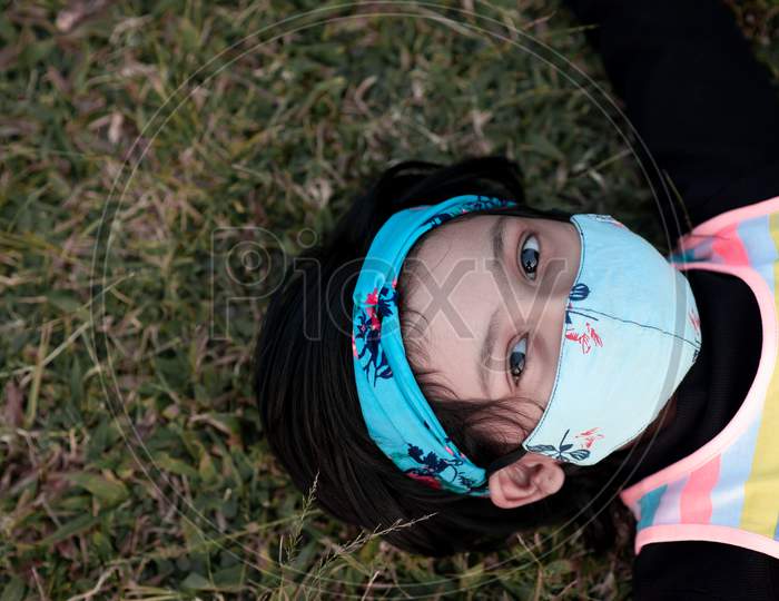 kid girl lying on grass with focus on face wearing a mask