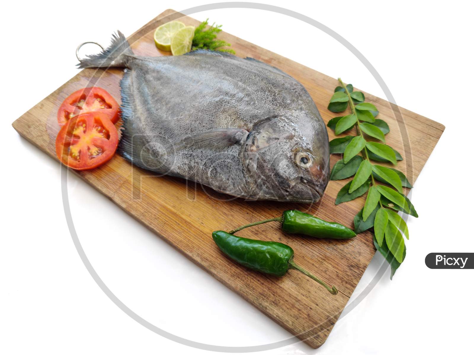 Fresh Black Pomfret Fish Decorated With Herbs And Vegetables On A Wooden Pad,Selective Focus.