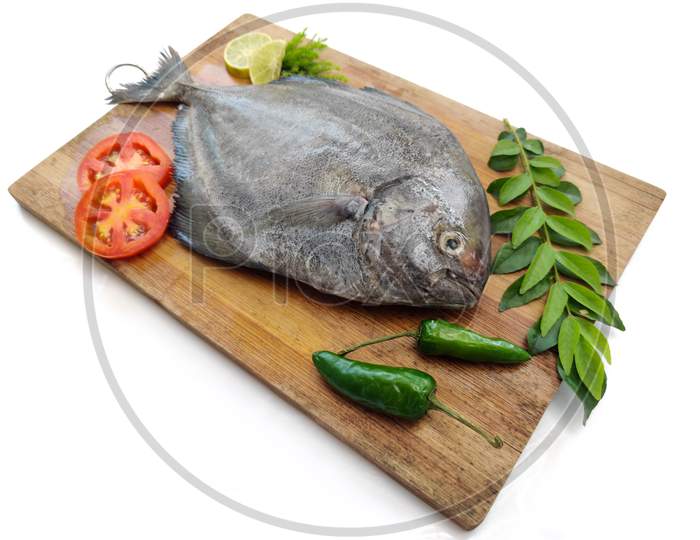Fresh Black Pomfret Fish Decorated With Herbs And Vegetables On A Wooden Pad,Selective Focus.