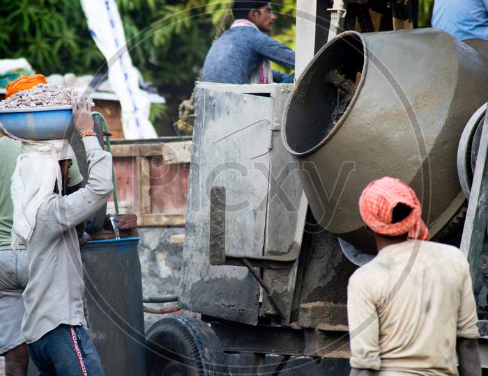Zoomed In Shot Of Indian Underprivleged Construction Workers Carrying Sand, Cement, Stones And Water On Their Head To Load Into A Mixer To Make Concrete For The Making Of Infrastructure Real Estate, Homes And Offices In India