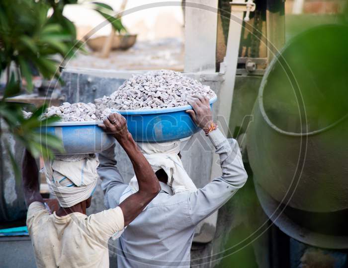 Zoomed In Shot Of Indian Underprivleged Construction Workers Carrying Sand, Cement, Stones And Water On Their Head To Load Into A Mixer To Make Concrete For The Making Of Infrastructure Real Estate, Homes And Offices In India