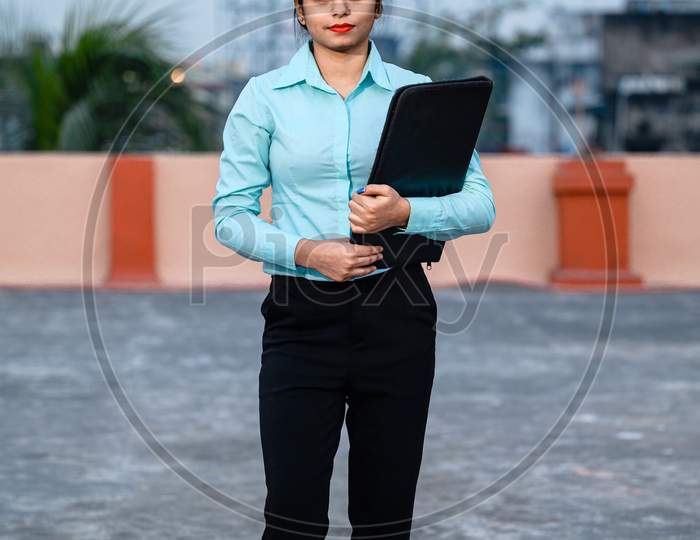 Full Length Portrait Of Beautiful Female Engineer Wearing A Protective Helmet And Holding Files In Hand While Looking At Camera.
