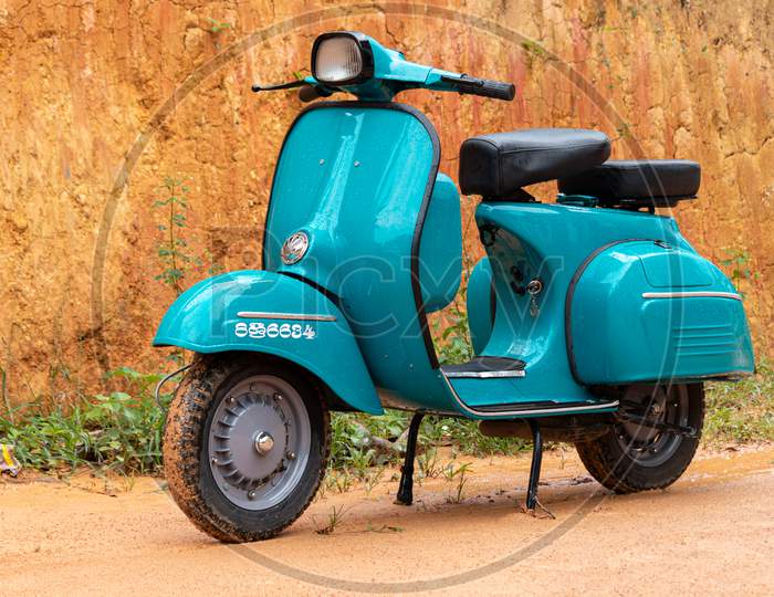 Old Vintage Blue Colored Scooter Bike On A Muddy Road, Front View.
