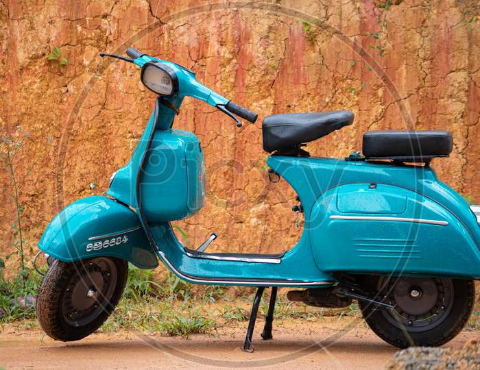 Old Vintage Scooter Motorbike In Display Against Clay Wall. Light Blue Color And Two-Seaters, Compartments For Storage, Round Headlamp In Front.