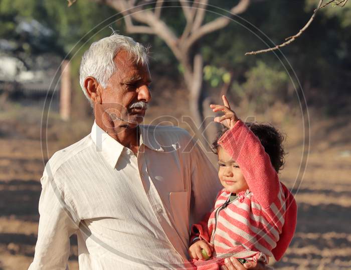 A Beautiful Indian Little Child Is Cropped By Hand And The Indian Grandfather Is Seen Cropping In The Garden