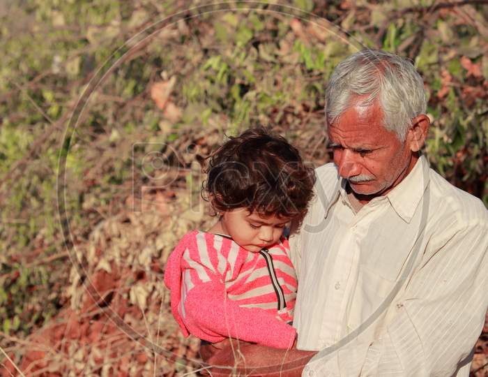 An Indian Small Child With An Indian Grandfather Sitting In The Grandfather'S Lap Enjoying Nature