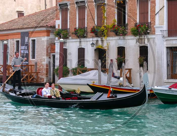 Gondolier Ferrying Passengers Along A Canal In Venice