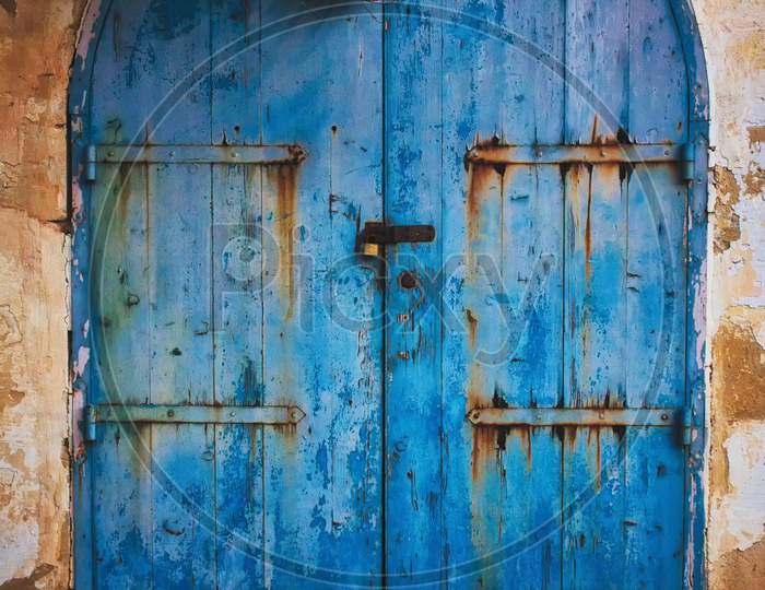 Old Blue Wooden Rustic Painted Door In The Countryside With Metal Hinges With Rust