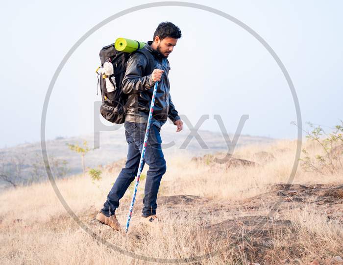 Side View Moving Wide Angle Shot Of Traveller With Backpack Hiking The Mountain By Holding Stick During Winter - Concept Of Solo Hiking Or Trekking.
