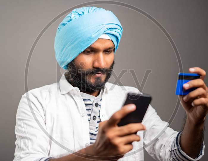 Young Sikh Man Purchasing By Paying Online Using Credit Card In Mobile Phone - Concept Of Online Shopping Or Ordering From E-Commerce.