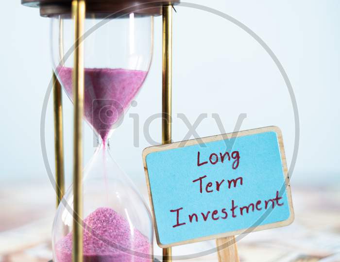 Sand Timer With Long Term Investment Sign Board On Currency Notes - Concept Of Future Financial And Retirement Plans.