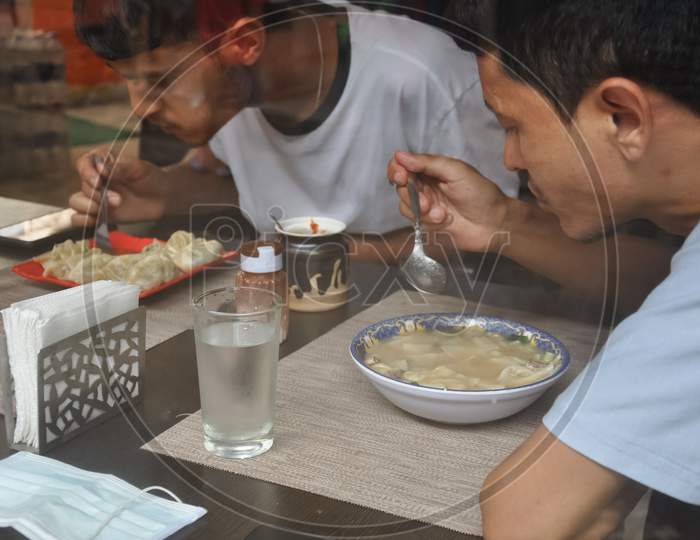 Two male friends eating tibetan food at indoor cafe seen through window glass