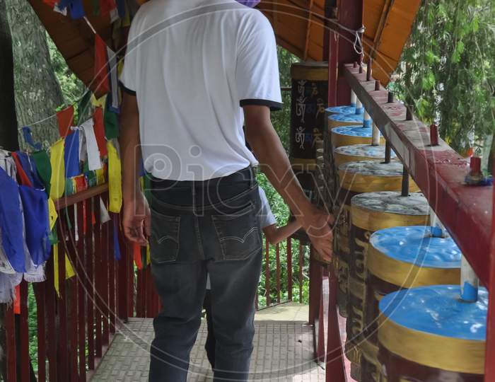 Back view of a young guy wearing face mask with turning Buddhist prayer wheel in Tso-Pema