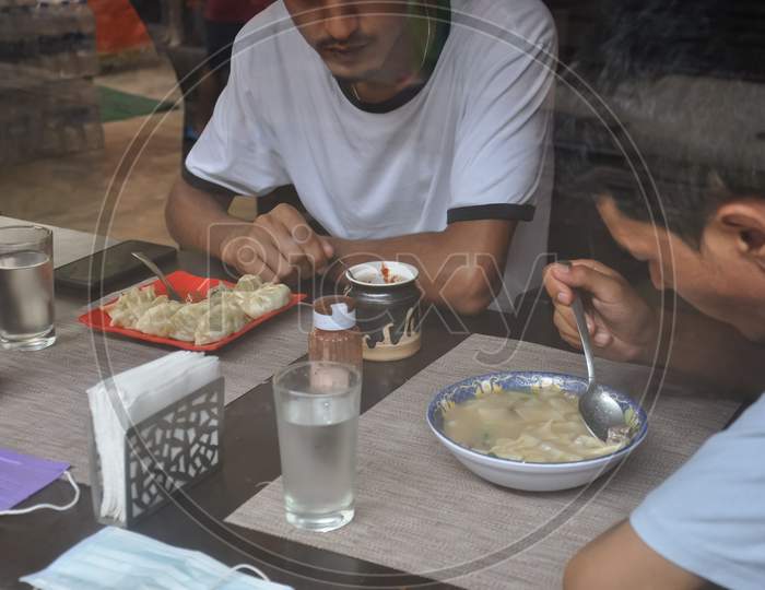 Selective focus of two young guys eating tibetan food at indoor cafe seen through window glass