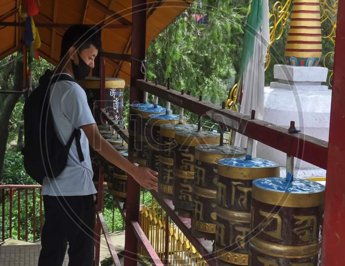 Back view of a Ladakhi young guy wearing face mask with turning Buddhist prayer wheel in Tso-Pema