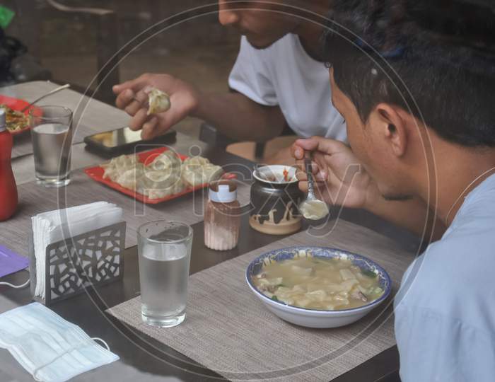 Selective focus of two young guys eating tibetan food at indoor cafe seen through window glass