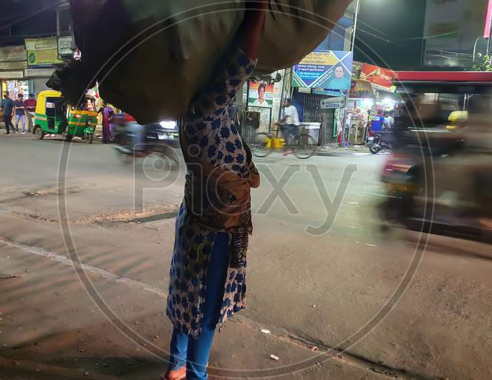 A Ragpicker girl carries huge bag of rags on her head in a street at kolkata, India.