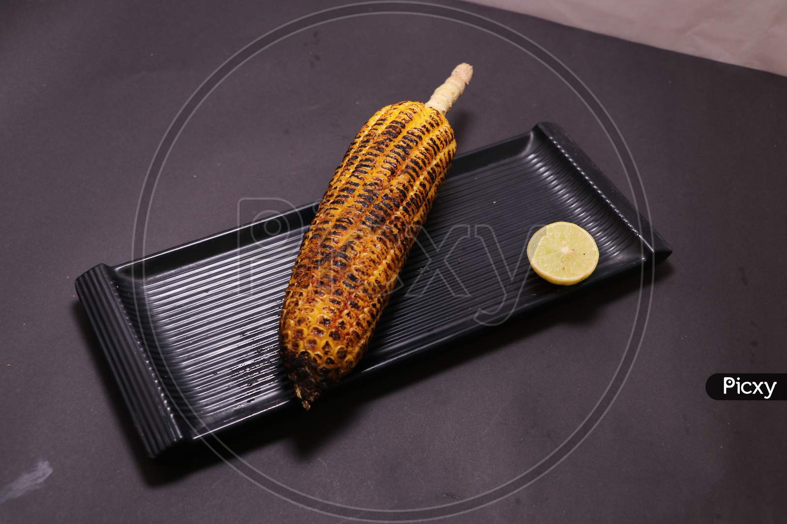 Rosted sweet corn bhutta with lemon in black plate