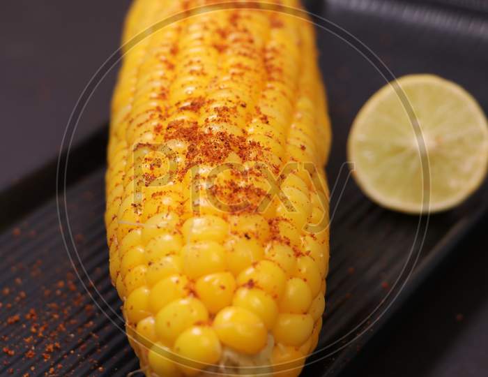 Sweet Corn bhutta with lemon with red chatni in black plate