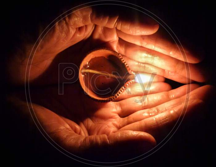 Women hand holding a diya or pradeep or oli lamp on dark background on the occasion of Diwali festival of lights in India