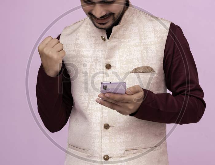 Handsome Boy Wearing On Isolated Background Showing Strong Positive Emotions While Holding Cellphone In Her Hand, Having Received Extraordinary Great News From Web Or Mates. Happiness.