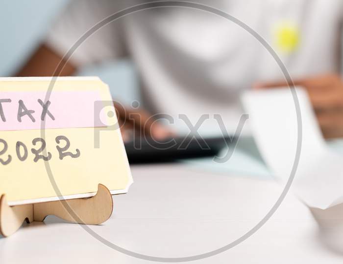Focus On Tax 2022 Sign Board, Unrecognizable Man Calculating Expense Or Bills Behind The Tax 2022 Sign Board - Concept Of Finance, Banking And Accounting Management