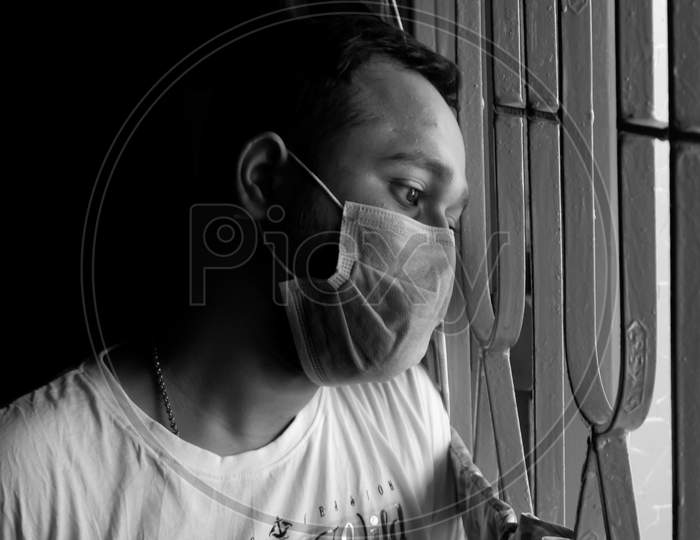 Black And White Image Of Boy With Mask On Face Watching Out Of The Window To Outside Of World With Stressful Expression.