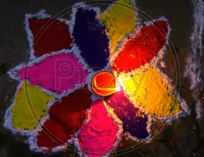 Closeup photo of a rangoli with a clay diya lighting up in the centre of it.