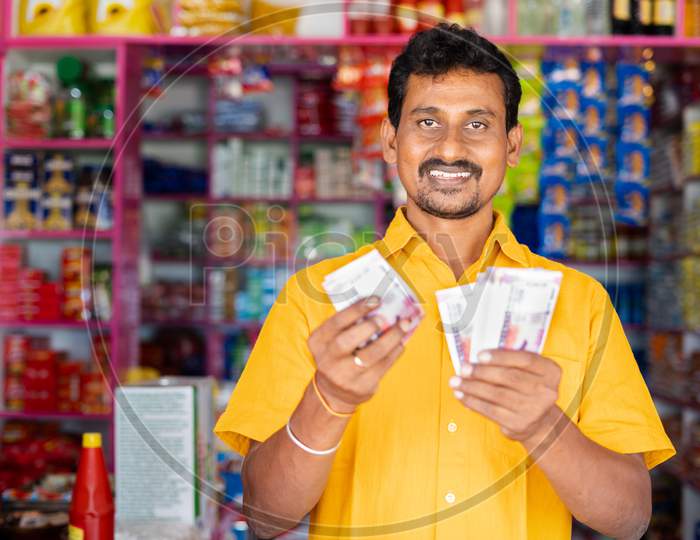 Happy Smiling Groceries Or Kirana Merchant Small Business Owner Counting Money By Looking At Camera - Concept Of Successful Business, Profit Making, Banking And Finance.