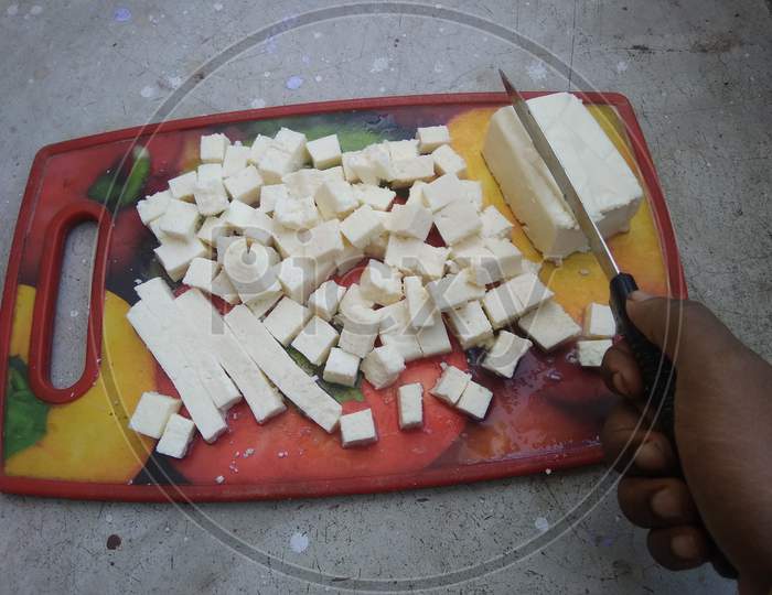 Paneer, cheese cutting with knife on colorful chopping board