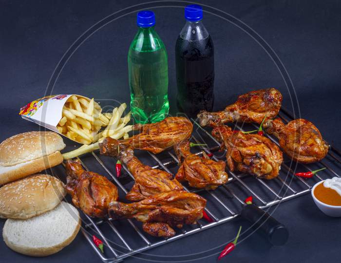 Hot And Crispy Grilled Chicken Legs Isolated On A Grill Platter.French Fries, Cold Drink And In Background