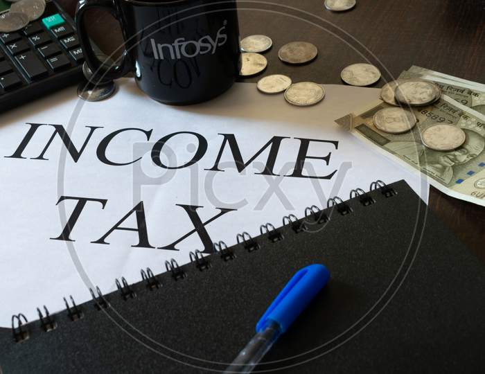 Mumbai, India - 19 October 2021, Picture of Income tax written on a page along with calculator, diary, cash, pen and a cup on which Infosys is written to show their collaboration.