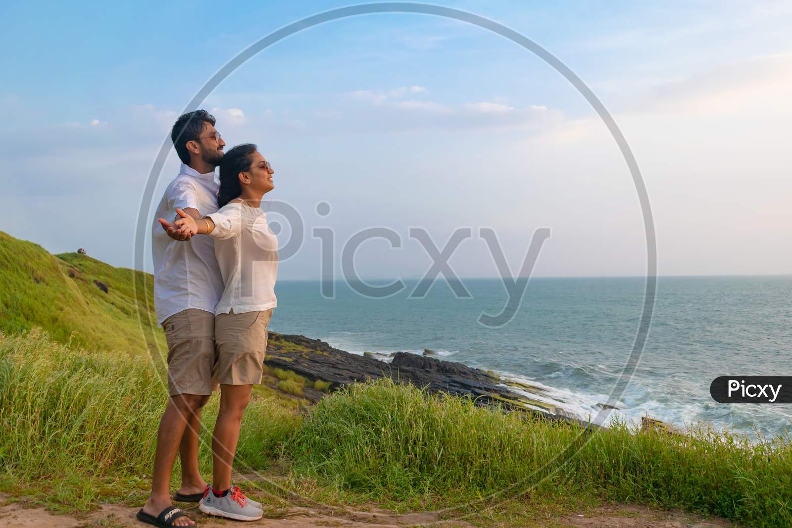 Goa, India - 02 October 2021, Picture of a young tourist couple enjoying their time on cliff above sea with grass around, near beach, post corona or covid19 lockdown